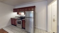 This single-floor unit offers a functional and comfortable layout with a variety of notable interior details throughout. The main living area is spacious and open, featuring warm hardwood-style flooring that flows seamlessly through the space. Crown molding frames the room, adding a classic touch, while a textured ceiling provides additional character. White walls keep the area bright and neutral, offering a versatile canvas for any style.

The kitchen is well-appointed with rich, dark wood cabinetry offering generous storage, dark granite-style countertops, and a full suite of stainless steel appliances including an electric range with overhead ventilation, a full-size refrigerator, and a sink. Light tile flooring in the kitchen provides a clean, practical surface that complements the cabinetry.

The bathroom features a retro-inspired design with distinctive terracotta-toned wall tiles surrounding a full shower and tub combination. A window above the tub allows for natural light, while classic mosaic-style tile flooring and a drop-in ceiling complete the look.

Additional highlights include a closet accessible from the living area, a tiled entryway near the front door, and well-maintained white trim and baseboards throughout, contributing to a clean and cohesive aesthetic across the entire space.