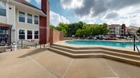 Located at 11502 Craig Ct in Saint Louis, Missouri, this outdoor amenity space serves as a central gathering area designed for relaxation and recreation. The centerpiece is a generously sized, freeform swimming pool with a gradual stepped entry and clearly marked shallow depths, set within a wide, open concrete deck that provides ample room for sunbathing and socializing.

The surrounding deck is well-appointed with multiple lounge chairs and chaise seating arranged throughout, offering plenty of space to unwind under the open sky. A wooden pergola structure adds architectural character to the area and provides a shaded spot alongside a charcoal grill, making it well-suited for outdoor gatherings. A separate seating area with a table, chairs, and a colorful umbrella offers an additional space for casual outdoor dining or conversation.

The entire pool area is enclosed by a sturdy black iron fence with a gated entry, ensuring privacy and security. Mature trees line the perimeter, providing natural shade and a lush green backdrop. The surrounding multi-story brick and siding residential buildings frame the space, creating a communal feel. Natural light floods the area, and the open sky above enhances the bright, welcoming ambiance of this well-maintained outdoor retreat.
