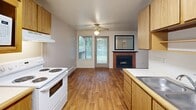 Located in Lakewood, Washington, this one-bedroom, one-bathroom unit offers a practical and comfortable single-floor layout. The kitchen is efficiently designed with warm wood cabinetry in mixed light and dark tones, white appliances including a coil-top range, built-in microwave, and refrigerator, complemented by light countertops and hardwood-style flooring. A skylight overhead brightens the space naturally. The open living and dining area extends from the kitchen and features the same hardwood-style flooring, a ceiling fan, a sliding glass door that fills the room with natural light and provides outdoor access, and a charming brick fireplace with a decorative mantel mirror — a notable focal point of the space. The bedroom offers plush carpeting, a large window with views of surrounding greenery, a baseboard heater, and a generous built-in closet with bifold doors providing ample storage. The bathroom is clean and straightforward, featuring a full tub-shower combination with a curtain rod, a wood-vanity with under-sink storage, and matching hardwood-style flooring. Neutral tones and warm wood accents throughout give the unit a cohesive, welcoming feel.