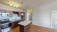 This single-floor residence offers a thoughtfully designed layout that balances functionality and style throughout its living spaces. The kitchen serves as a central highlight, showcasing rich dark wood cabinetry extending to the ceiling, light granite countertops, and a full suite of stainless steel appliances including a range, microwave, refrigerator, and dishwasher. A built-in wine rack adds a distinctive touch above the sink, while pendant lighting suspended from a track fixture illuminates the space. A granite-topped central island provides additional workspace and serves as a natural transition into the adjacent living area.

The living room benefits from generous natural light streaming through a bank of windows flanking an exterior door, complemented by warm hardwood-style flooring and a ceiling fan overhead. Bedrooms feature plush carpeting, ceiling fans, and windows that bring in ample daylight. The bathroom includes a full tub-shower combination with clean white surrounds, a dark granite vanity top, and wood-style flooring that ties back to the main living areas. Neutral wall tones throughout create a cohesive, understated palette, while consistent finishes across rooms contribute to an overall sense of continuity and comfort.