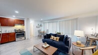 This single-floor residence is thoughtfully designed with a functional, open layout that seamlessly connects the main living spaces. The living room serves as the centerpiece, featuring light wood-style flooring, white walls, and a generous wall of floor-to-ceiling vertical blinds that allow ample natural light to fill the space. A private entry door opens directly into this area, which flows naturally into both the dining space and kitchen.

The kitchen is well-equipped with rich cherry wood cabinetry, granite countertops, a subway tile backsplash, and a full suite of stainless steel appliances, including a gas range, dishwasher, and refrigerator. Recessed lighting adds a polished finish. The adjacent dining area comfortably accommodates a four-person table and benefits from the same natural light as the living room.

The bedroom is a comfortable retreat with soft carpet flooring, a vertical blind-covered window, and direct access to both a closet and the bathroom. The bathroom features a granite-topped vanity with an undermount sink, warm-toned cabinetry, and a shower-tub combination. Throughout the residence, the neutral color palette and consistent finishes create a cohesive, welcoming ambiance.