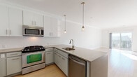 Located at 1 Willett Ave in Port Chester, NY, this single-floor residence offers a thoughtfully designed open layout with contemporary finishes throughout. The kitchen is a standout feature, outfitted with stainless steel appliances including a gas range, microwave, refrigerator, and dishwasher. Two-toned cabinetry pairs white upper cabinets with grey lower cabinets against a classic white subway tile backsplash. A peninsula with a quartz-style countertop and undermount sink serves as both a functional workspace and a natural divider between the kitchen and living area. Pendant lighting adds a modern touch overhead. The living area is bathed in natural light, with light hardwood flooring and crown molding lending an elegant finish. A full-width sliding glass door opens to a private balcony, offering views of the surrounding Port Chester neighborhood. The bedroom features plush carpeting, neutral walls, and a double window that brings in additional natural light. The bathroom is finished in a clean, modern style with large-format tile flooring, a white vanity, and a full soaking tub with a tiled surround. Throughout the space, a neutral color palette and consistent design elements create a cohesive and inviting atmosphere.