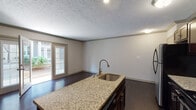Located at 1027 Everett Ave in Louisville, Kentucky, this single-floor residence offers a well-designed layout with a blend of modern finishes and functional living spaces. The kitchen serves as a central highlight, featuring rich dark cabinetry, granite countertops, a central island with a stainless steel sink, subway tile backsplash, and a full suite of stainless steel appliances including a refrigerator, range, and microwave. Track lighting adds a contemporary touch overhead. Dark hardwood flooring extends throughout the main living areas, lending a warm and polished aesthetic. The living area is bright and open, benefiting from natural light that pours in through a set of elegant French doors, which provide direct access to an outdoor patio space — ideal for indoor-outdoor living. A carpeted bedroom offers a quieter, cozier atmosphere, complete with a window fitted with blinds for natural light and privacy. The bathroom is finished with classic white subway tile surrounding the tub and shower, accented by a decorative mosaic tile inlay, chrome fixtures, and clean, neutral tones throughout. Textured ceilings and crown molding details are consistent across the space, contributing to a cohesive and tidy interior character.