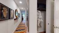 This two-floor residence is thoughtfully designed with a clean, contemporary aesthetic carried consistently across both levels. Wood flooring runs throughout the main living areas, complementing the neutral color palette and recessed lighting that brightens each room. The living area is anchored by a glass door that opens directly to a private outdoor space with a wood-slatted privacy screen, allowing natural light to fill the interior. The kitchen is equipped with stainless steel appliances, including a French door refrigerator, slide-in range with an over-the-range microwave, and dark cabinetry paired with a light subway tile backsplash.

The hallway connecting the main spaces features a decorative mirror, wall shelving, and a colorful runner rug, leading to an open closet with built-in shelving and hanging storage. Two well-proportioned bedrooms each feature wood floors, wall-mounted climate control units, and windows that provide natural light. The bathrooms are finished with white cabinetry, dark stone-topped vanities, and tiled tub-shower combinations. A separate half bath offers additional convenience. The overall layout is efficient and well-organized across both floors.