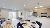 This thoughtfully designed single-floor residence in Jackson, NJ offers a seamless blend of modern aesthetics and functional living. The open-concept layout connects the living, dining, and kitchen areas into a cohesive, airy space bathed in natural light from sliding glass doors that lead to a private balcony with outdoor views.

The living room features warm hardwood-style flooring, recessed lighting, and a welcoming atmosphere anchored by a curved navy sofa, framed wall art, and a wall-mounted flat-screen TV. The dining area accommodates a round table with ample seating, positioned for easy flow between the kitchen and living spaces.

The contemporary kitchen is outfitted with flat-front light wood cabinetry, white countertops, stainless steel appliances including a gas range, microwave, and refrigerator, and a double-basin sink — all illuminated by overhead panel lighting.

The bedroom is a calm retreat with neutral walls, hardwood-style flooring, and natural light from a large window. It includes a well-organized walk-in closet with built-in shelving and hanging rods for generous storage.

The bathroom is finished in clean, light-toned tile throughout, featuring a soaking tub with a glass enclosure, a floating wood vanity, and recessed lighting, delivering a spa-like experience. In-unit laundry is also conveniently accessible within the home.