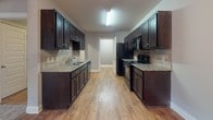 Located at 3085 Commonwealth Dr in Spring Hill, Tennessee, this single-floor residence offers a well-appointed layout designed for comfortable everyday living. The galley-style kitchen is a standout feature, showcasing rich dark cabinetry, granite countertops, a tile backsplash, double-basin sink, and black appliances including a gas range and refrigerator — all set atop warm hardwood-style flooring. The kitchen flows into a dining area illuminated by an elegant chandelier. The living area impresses with soaring vaulted ceilings, plush carpeting, and French doors that invite natural light. Bedrooms are carpeted and generously sized, each equipped with ceiling fans and closet space, with one bedroom featuring a walk-in closet and direct access to a private bathroom. Two full bathrooms are present throughout the home, each featuring dark vanity cabinetry with granite countertops, hardwood-style flooring, and tub-shower combinations with brushed nickel fixtures. Neutral gray wall tones are carried consistently throughout, creating a cohesive and modern aesthetic. The overall design balances practicality with refined finishes, making this Spring Hill residence a well-rounded and move-in-ready home.