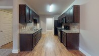 Located at 3085 Commonwealth Dr in Spring Hill, Tennessee, this single-floor residence offers a well-appointed layout designed for comfortable everyday living. The galley-style kitchen is a standout feature, showcasing rich dark cabinetry, granite countertops, a tile backsplash, double-basin sink, and black appliances including a gas range and refrigerator — all set atop warm hardwood-style flooring. The kitchen flows into a dining area illuminated by an elegant chandelier. The living area impresses with soaring vaulted ceilings, plush carpeting, and French doors that invite natural light. Bedrooms are carpeted and generously sized, each equipped with ceiling fans and closet space, with one bedroom featuring a walk-in closet and direct access to a private bathroom. Two full bathrooms are present throughout the home, each featuring dark vanity cabinetry with granite countertops, hardwood-style flooring, and tub-shower combinations with brushed nickel fixtures. Neutral gray wall tones are carried consistently throughout, creating a cohesive and modern aesthetic. The overall design balances practicality with refined finishes, making this Spring Hill residence a well-rounded and move-in-ready home.