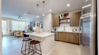Located at 2410 Canopy Breeze Cir in Orlando, Florida, this single-story residence offers a thoughtfully designed open-concept layout with contemporary finishes throughout. Light wood-tone flooring flows seamlessly across the entire space, creating a cohesive and airy aesthetic.

The kitchen is a standout feature, equipped with stainless steel appliances including a french-door refrigerator, range, microwave, and dishwasher. Warm wood cabinetry is complemented by open shelving, a herringbone-patterned tile backsplash, and crisp white quartz countertops. A central island with seating for two pendant globe lights above serves as the hub connecting the kitchen to the living area.

The living room is bright and welcoming, with large windows and a glass sliding door that invites abundant natural light. Neutral walls provide a versatile backdrop for curated décor accents.

The bedrooms are generously proportioned, each offering ample natural light via well-positioned windows, ceiling fans, and a calm, neutral color palette. The bathroom is cleanly finished with a wood-toned floating vanity, quartz countertop, a large framed mirror, and a full tub-shower combo with white subway tile surround. Every room reflects a cohesive modern design sensibility suited for comfortable living in Central Florida.