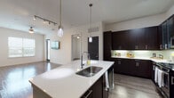 This thoughtfully designed single-floor residence combines modern aesthetics with functional living. The open-concept kitchen serves as the heart of the home, featuring a large center island with a white quartz countertop and undermount double sink, bold dark espresso cabinetry extending to the ceiling, stainless steel appliances including a French door refrigerator and gas range, and elegant glass pendant lighting overhead. Track lighting and under-cabinet illumination further enhance the kitchen's polished look, while wood-look flooring flows seamlessly into the adjacent living area. The bedrooms are bright and welcoming, each benefiting from natural light through large windows dressed with horizontal blinds and ceiling fans for year-round comfort. One bedroom connects directly to a walk-in closet, adding practical storage. The bathrooms are finished with the same attention to detail — the primary bath offers a dual-sink vanity with white quartz counters and dark cabinetry, while a secondary bath includes a tiled soaking tub and shower combination with a full-width mirror above the vanity. Consistent use of wood-look flooring, crisp white walls, and dark accent doors and cabinetry throughout creates a cohesive, contemporary ambiance across the entire residence.
