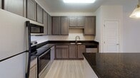 Located at 10 Newbridge Pkwy in Woodfin, North Carolina, this single-floor residence offers a well-designed layout that balances functionality with modern finishes throughout. The kitchen serves as a central highlight, showcasing rich dark granite countertops that extend across a peninsula island, complemented by warm taupe cabinetry with ample storage. Stainless steel appliances — including a refrigerator, range, microwave, and dishwasher — complete the space, while pendant lighting adds a refined touch. Light wood-style flooring runs through the kitchen and connects seamlessly to adjacent areas. The living and bedroom spaces feature plush wall-to-wall carpeting and neutral tones that lend a calm, versatile ambiance. A large window in the main living area allows generous natural light and provides views of the surrounding landscape. The bathroom is equipped with a walk-in shower, a vanity with stone-look countertop, and blue-toned cabinetry paired with light wood flooring for a clean, contemporary feel. A dedicated laundry room with wire shelving, washer/dryer hookups, and dryer venting adds practical convenience. Clean lines, neutral walls, and consistent finishes throughout create a cohesive and move-in-ready environment.