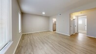 Located at 400 Cox Landing in Newport News, Virginia, this single-floor residence offers a thoughtfully updated interior with a clean, modern aesthetic. Light neutral tones and white trim carry throughout the home, creating a cohesive and welcoming atmosphere.

The open living area is bright and airy, featuring light wood-look luxury vinyl plank flooring and multiple windows that invite natural light. The space flows seamlessly toward the kitchen, which stands out as a key feature of the home. The kitchen is equipped with white cabinetry accented by matte black hardware, granite-look countertops, a stainless steel range and dishwasher, and a stainless refrigerator — all contributing to a polished, functional workspace.

The bedroom offers a comfortable retreat with plush wall-to-wall carpeting, neutral walls, and a window with blinds providing natural light and privacy. A closet with louvered doors provides convenient storage.

The bathroom continues the home's modern design language with white cabinetry, a framed mirror, a white countertop vanity, and matte black fixture accents. The floor plan, as seen in the 3D overview, reveals a well-organized single-level layout that maximizes the use of space across living, sleeping, cooking, and bathing areas.