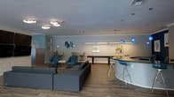 This single-floor space offers a well-appointed communal lounge designed for both casual relaxation and social interaction. The open-plan layout is anchored by warm wood-look flooring and a neutral color palette accented by soft teal and blue tones throughout.

The seating area features plush gray sectional sofas and teal accent chairs arranged to encourage conversation, complemented by a sleek white side table. Nearby, a high-top curved bar counter with chrome barstools serves as a central gathering point, illuminated by striking cobalt blue pendant lights that add a bold design touch.

A shuffleboard table occupies the middle of the room, providing an entertaining focal point for recreational use. Additional high-top seating with slender bar chairs can be found along the perimeter, offering flexible arrangements for smaller groups.

The walls are adorned with colorful framed artwork that adds visual interest and a contemporary feel to the space. Recessed lighting and flush-mount ceiling fixtures ensure the room is well-lit throughout. Subtle architectural details such as tray ceiling transitions and clean crown molding contribute to the polished, modern aesthetic. Overall, the space strikes a balance between inviting comfort and stylish functionality.