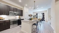 Located in Grand Prairie, TX, this one-bedroom, one-bathroom residence offers a thoughtfully designed open-concept layout that maximizes every square foot of its single-floor plan. The combined kitchen and living area serves as the heart of the home, anchored by a spacious granite-topped island with bar seating — ideal for casual dining or meal prep. The kitchen is outfitted with rich dark cabinetry, a white subway tile backsplash, stainless steel appliances including a refrigerator, microwave, and range, and a matte black faucet that adds a contemporary touch. Light wood-style flooring flows throughout the main living areas, complementing the bright, white walls and recessed lighting. A modern sputnik chandelier adds a striking design focal point overhead. The living area offers comfortable, open space with natural light filtering in through large windows dressed with bold decorative curtains. The bedroom features plush carpeting, generous natural light from a large window, and sufficient space for a full furniture arrangement. A dedicated closet and a full bathroom — complete with a soaking tub, shower, and tile surround — round out this efficiently designed and stylishly finished residence.