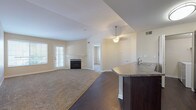 This single-floor residence offers a thoughtfully designed open-concept layout that seamlessly connects the living, dining, and kitchen areas. The living room is a welcoming space anchored by a classic fireplace with a white mantel, complemented by neutral-toned carpet and a pendant light fixture overhead. Natural light filters in through blinds-covered windows, adding warmth to the space.

The kitchen is outfitted with dark espresso cabinetry, granite-style countertops, and stainless steel appliances, including a refrigerator, electric range, and over-the-range microwave. A raised breakfast bar peninsula serves as a functional divider between the kitchen and living areas. Dark hardwood-style flooring runs throughout the kitchen and dining zone, creating a clean contrast with the carpeted living spaces.

The bedrooms are generously sized, featuring plush carpet, vaulted or standard ceilings depending on the room, and ample natural light from large windows with exterior views. The primary bedroom includes access to a walk-in closet area. The bathroom features a full soaking tub with tiled surround, dark vanity cabinetry with granite-style countertops, and hardwood-style flooring. A dedicated in-unit laundry area adds everyday convenience.
