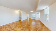 This three-floor townhome at 4500 New Linden Hill Rd in Wilmington, Delaware offers a well-organized layout designed for comfortable everyday living. Warm hardwood-style flooring flows throughout the main and upper levels, creating a cohesive and inviting aesthetic across the home.

The main living level is notably open and expansive, with generous natural light streaming through multiple windows. The space transitions seamlessly from a broad living area into a well-appointed kitchen featuring white shaker-style cabinetry, granite countertops, stainless steel appliances — including a refrigerator, range, and microwave — and a sink with an adjacent window. The open-concept design promotes an easy flow between cooking, dining, and living areas.

Stairways with wooden treads and handrails connect all three levels. The upper floor hosts additional living or bedroom spaces, including a bright room with dual windows offering views of the surrounding greenery. A full bathroom on this level includes a double-sink vanity with white cabinetry, a large mirror, and hardwood-style flooring.

The lower level provides utility access, housing the HVAC system and water heater in a functional utility room with a concrete floor, insulated walls, and a window. Clean white walls and crisp trim throughout all levels contribute to a fresh, move-in-ready appearance.