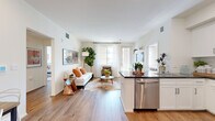 Located at 1900 E Inland Empire Blvd in Ontario, CA, this 2-bedroom, 2-bathroom single-floor residence offers a well-designed open-concept layout that seamlessly connects the kitchen, dining, and living areas. The kitchen is outfitted with stainless steel appliances — including a gas range, microwave, and full-size refrigerator — complemented by white shaker cabinets, a subway tile backsplash, and a dark quartz peninsula that doubles as a breakfast bar. Wood-style flooring flows throughout the main living areas, enhancing the bright, airy atmosphere created by large windows dressed with sheer curtains. The living room provides a comfortable, light-filled retreat with direct access to natural light. The primary bedroom is a well-proportioned private space, while the second bedroom features a glass door that invites additional natural light. Both bathrooms are finished with light tile flooring and white vanities with dark countertops; one includes a shower-tub combo with subway tile surround and built-in shelving. Each bedroom is served by its own dedicated closet. A connecting hallway ties the layout together efficiently, making this a functional and stylish single-level residence.