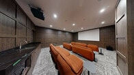 Located at 422 Cherry Street in Toronto's vibrant Corktown neighbourhood, this dedicated screening room offers a refined and immersive cinematic experience. The space is thoughtfully designed with floor-to-ceiling dark wood wall panelling that lends a warm, sophisticated ambiance throughout. Three rows of bold burnt-orange leather lounge sofas are arranged in a theatre-style layout, each accompanied by individual side tables for added convenience. A large projection screen anchors one end of the room, paired with a ceiling-mounted projector and in-ceiling speakers that ensure an enveloping audio-visual experience. Recessed pot lighting illuminates the space evenly, complementing the rich tones of the wood panelling. A small kitchenette with a dark stone countertop, sink, and microwave is tucked discreetly at the rear, making the room well-equipped for extended gatherings. The floor is finished with a textured grey carpet that adds comfort underfoot while contributing to the room's acoustic quality. This screening room combines upscale design with practical amenities, making it an ideal venue for private movie screenings or entertainment events.
