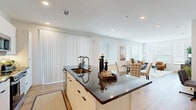 This thoughtfully designed 2-bedroom, 3-bathroom single-floor residence offers a seamless open-concept layout that connects the kitchen, dining, and living areas into one cohesive, light-filled space. The modern kitchen is a standout feature, showcasing crisp white cabinetry that extends to the ceiling, stainless steel appliances, and a large central island topped with dark granite countertops that doubles as a breakfast bar with leather-upholstered stools. The open dining area flows naturally into the bright living room, where light wood-look flooring, large windows with horizontal blinds, and a sliding door with vertical blinds invite abundant natural light throughout the day. The primary bedroom is a serene retreat, carpeted for comfort and fitted with a ceiling fan, multiple windows, and access to a dedicated closet with full rod-and-shelf storage systems. The second bedroom mirrors this warmth with carpet flooring, generous natural light, and its own ceiling fan. The bathrooms feature elegant tile work, including a shower with floor-to-ceiling linear stone-look tile and a glass enclosure. Two well-organized closets provide ample storage throughout the residence, completing this functional and contemporary living space.