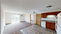 Located at 1000 Opportunity Blvd S in Cambridge, Minnesota, this single-floor residence offers a well-designed, functional layout with a comfortable and practical living environment. The open-concept living and dining area is finished with plush wall-to-wall carpeting and transitions seamlessly into the kitchen via durable stone-look tile flooring. A chandelier overhead adds a subtle decorative touch to the shared space, while a sliding glass door fills the living area with natural light and leads to a private balcony overlooking the surrounding greenery. The kitchen is efficiently arranged with rich warm-toned wood cabinetry, dark granite-style countertops, and a full suite of white appliances including a refrigerator, electric range, microwave, and dishwasher. The bedrooms are carpeted and generously sized, with at least one featuring a walk-in closet with built-in shelving. The primary bathroom includes a double-sink vanity with a wide mirror, a tub-shower combination, and matching tile flooring. A second full bathroom offers similar finishes in a more compact layout. A dedicated in-unit laundry room with a full-size washer and dryer adds everyday convenience. Baseboard heating and a wall-mounted air conditioning unit ensure year-round comfort throughout the home.