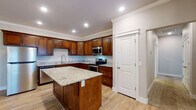Located at 941 Broyles St in Farmington, Arkansas, this single-story home offers a well-designed layout with quality finishes throughout. The kitchen serves as a standout feature, showcasing rich dark wood cabinetry, granite countertops, and a central island ideal for meal prep or casual dining. Stainless steel appliances — including a refrigerator, range, microwave, and dishwasher — complete the space, while light wood-look flooring and recessed lighting add a clean, modern touch. Crown molding lines the kitchen ceiling, lending an elevated architectural detail. The open doll-house view reveals a spacious living area adjacent to the kitchen, also finished with light hardwood-style flooring. The bedrooms feature plush carpeting, vaulted ceilings with ceiling fans, and natural light from window coverings. Each bedroom includes a well-organized walk-in or reach-in closet with built-in shelving. The primary bathroom is appointed with a dual-sink vanity, granite countertops, dark wood cabinetry, and large-format tile flooring, while a secondary bathroom includes a full tub and shower combination with brushed nickel fixtures. Throughout the home, neutral tones and consistent finishes create a cohesive and inviting atmosphere.