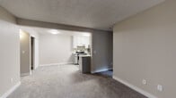 Located at 50 Austin Ave in Hayward, California, this single-floor unit offers a thoughtfully designed layout that balances functionality and comfort. The open living area is finished with plush carpeting and neutral warm-toned walls, creating a welcoming atmosphere throughout. Flush-mount ceiling lighting illuminates the space, which flows naturally into the kitchen through an open pass-through design.

The kitchen is a standout feature, outfitted with crisp white upper cabinetry, two-toned grey lower cabinets, and granite-style countertops. Stainless steel appliances include an electric range with oven, a refrigerator, and an under-cabinet range hood, all complemented by light wood-style vinyl flooring and a single-basin sink with a modern gooseneck faucet.

The bedrooms are generously proportioned, each carpeted and bathed in natural light from large windows that offer views of the surrounding exterior. One room features a sliding glass door that leads to a private balcony, adding an outdoor connection to the living space.

The bathroom is clean and functional, featuring a full-size soaking tub with an integrated shower, brushed nickel fixtures, a wall-mounted grab bar, and durable wood-look vinyl flooring. The textured ceilings throughout add a classic residential character to the overall design.