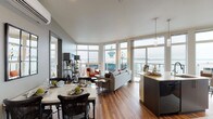 This thoughtfully designed single-floor residence combines contemporary architecture with sweeping waterfront and cityscape views, achieved through an extensive arrangement of floor-to-ceiling windows that flood every room with natural light. Warm hardwood flooring flows consistently throughout, unifying the open-concept layout.

The living area serves as the heart of the home, where oversized windows frame panoramic views of the water and surrounding skyline. The space transitions seamlessly into a dedicated dining area, complete with a marble-topped table and a wall-mounted mini-split system for climate control. A decorative mirror and framed artwork add character to this intimate setting.

The kitchen is sleek and functional, featuring dark flat-front cabinetry, light countertops, black appliances, and additional windows offering water views—making it as visually appealing as it is practical.

Both bedrooms are generously proportioned, each showcasing large windows that capture either waterfront or urban vistas. The primary bedroom features a calming blue accent wall and direct access to natural light on multiple sides.

Two bathrooms serve the residence; one offers a tub-shower combination with modern vanity cabinetry, while the second features a long double-sink vanity with clean, neutral finishes. The overall ambiance is polished, bright, and urban.