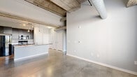 Located in the heart of Indianapolis on E Market St, this 3-bedroom, 2-bathroom urban loft blends industrial character with modern finishes across a well-planned single-floor layout. The open-concept kitchen and living area serves as the centerpiece of the space, showcasing exposed concrete beam ceilings, suspended ductwork, and polished concrete floors that extend throughout. The kitchen is equipped with dark cabinetry, black appliances, track lighting, and a striking stainless steel island with a built-in sink, illuminated by sleek pendant lights. Large windows and a sliding glass door in the living area flood the space with natural light and provide access to a private balcony with city views. Each of the three bedrooms features concrete flooring and exposed industrial ceiling elements, with some rooms showcasing raw concrete accent walls for added texture. The two bathrooms are finished with dark vanity cabinetry, granite-style countertops, and clean white fixtures. Additional conveniences include six closets and a dedicated laundry area, offering ample storage throughout. The overall ambiance is distinctly urban and industrial, ideal for those who appreciate loft-style living in a vibrant downtown setting.