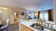 This well-appointed 2-bedroom residence is designed with a functional, open-concept layout that seamlessly connects the main living areas. The living room is a welcoming focal point, featuring a classic tile-surround fireplace with a white mantel, crown molding, and plush carpeting. French doors open to a private balcony or patio, allowing natural light to fill the space. Adjacent to the living room, a dedicated dining area provides space for a full dining set beneath pendant lighting, complemented by neutral-toned walls throughout.

The kitchen is efficiently laid out with light wood cabinetry, white appliances including a coil-top range and refrigerator, a double-basin sink, and a peninsula with bar seating that bridges the kitchen and living areas. A separate laundry area is also accessible from the kitchen.

The primary bedroom is generously sized, featuring multiple windows with blinds and curtain treatments, direct access to an exterior door, and soft carpeting. The accompanying bathroom includes a wide vanity with light wood cabinetry, a large mirror with above-mirror lighting, and a full tub/shower combination. A second bedroom and additional bathroom complete this single-floor layout.