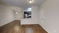 This single-floor residence offers a clean, modern aesthetic defined by an open-concept design that seamlessly connects the living area and kitchen. Rich hardwood-style flooring flows throughout the main living space, adding warmth and continuity to the layout. The kitchen is positioned centrally and features dark espresso cabinetry, stainless steel appliances including a refrigerator, range, and microwave, as well as a granite countertop peninsula that doubles as a breakfast bar and serves as a natural divider between the kitchen and living area. Recessed and pendant lighting accents the space, providing both functional illumination and decorative character. The living area is generously proportioned, offering ample room for a variety of furniture arrangements. Crisp white walls and white trim throughout give the space a bright, neutral canvas that is move-in ready and easy to personalize. A solid entry door with clean hardware provides a welcoming entry point. The overall ambiance is contemporary and well-maintained, combining practical functionality with stylish finishes that appeal to a modern lifestyle.
