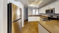 This single-floor residence offers a thoughtfully designed layout with a cohesive neutral color palette of warm grays and taupe tones throughout. The kitchen serves as a functional centerpiece, showcasing crisp white shaker-style cabinetry, rich brown countertops, and a full suite of stainless steel appliances including a refrigerator, electric range, over-the-range microwave, and dishwasher. A tray ceiling with track lighting adds architectural interest above, while warm hardwood-style flooring anchors the space with a welcoming feel. Natural light filters in through a window above the sink, brightening the room. The bedrooms are generously sized, each featuring plush carpeting, ceiling fans, and windows dressed with horizontal blinds. One bedroom offers access to an outdoor area through a sliding door with vertical blinds. The bathrooms are well-appointed with white vanity cabinetry, warm brown countertops, large mirrors with vanity lighting, and tiled tub-shower combinations. The overall design is clean and functional, presenting a comfortable and move-in-ready living environment with consistent finishes carried throughout every room.