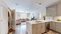 This single-floor residence at 1-5 Soldier Hill Road in Paramus, NJ, presents a thoughtfully designed open-concept layout finished with consistent wood-look flooring and a neutral color palette throughout. The kitchen serves as a central hub of the home, featuring taupe shaker-style cabinetry extending to the ceiling, quartz countertops with subtle veining, and a large peninsula with an undermount sink that opens directly to the living area. Stainless steel appliances, including a gas range, microwave, and French door refrigerator, complement the under-cabinet lighting and white tile backsplash.

The adjoining living area is generously proportioned, accommodating a large sectional sofa and media console with ease. Natural light enters through horizontal-blind-fitted windows, and a ceiling fan enhances comfort. A door from the living area provides access to an outdoor space. The bedroom is a calm retreat with carpeted flooring, natural light from a large window, and a serene neutral tone. A hallway connects the private areas, leading to a well-appointed bathroom featuring a dual-sink vanity with dark espresso cabinetry, quartz countertops, a large mirror, and a glass-enclosed shower.