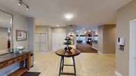 This single-story community clubhouse in Buffalo Grove, Illinois, is thoughtfully designed to provide a range of functional and social spaces. The entry area features light-toned tile flooring and flows seamlessly into the main gathering spaces beyond.

The central lounge is a standout area, anchored by a dramatic floor-to-ceiling brick fireplace with a white-mantled surround and a mounted flat-screen television. Flanking windows fill the room with natural light and outdoor views, while vaulted ceilings with elegant chandelier fixtures lend an airy, open feel. Plush seating arrangements invite relaxed conversation throughout the space.

A bar-height counter with seating connects the lounge to a fully equipped kitchen, which includes dark cabinetry, stainless steel appliances, tile flooring, and ample counter space—ideal for catering or community events.

A dedicated business center, accented by exposed brick columns and large windows, provides workstations and printing equipment. A cozy dining nook nearby, framed by wraparound windows overlooking the outdoor surroundings, offers a bright and intimate setting.

Additional flexible areas with carpeted flooring and French doors provide versatile spaces for meetings or gatherings. Neutral gray walls and consistent decorative accents tie the entire clubhouse together into a cohesive, welcoming environment.