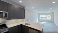 This contemporary apartment, part of The Lofts at Gloucester, offers a well-designed living space of 930 square feet. The floor plan includes two bedrooms and two bathrooms, with the primary bedroom measuring a generous 160 square feet. The open-concept layout creates a seamless flow between the living areas, enhancing the sense of space.

The kitchen is a standout feature, boasting dark wood cabinetry contrasting beautifully with stainless steel appliances and white countertops. It's equipped with a gas range, built-in microwave, and a side-by-side refrigerator, perfect for culinary enthusiasts.

Both bathrooms showcase modern design with large vanities, ample storage, and glass-enclosed showers. The dark wood cabinetry in the bathrooms echoes the kitchen's aesthetic, creating a cohesive design throughout the apartment.

Large windows in the bedrooms and living area flood the space with natural light, while also offering views of the surroundings. The light-colored walls and grey wood-look flooring contribute to the bright, airy feel of the apartment.

Storage is well-considered, with built-in closets featuring dark wood finishes that match the overall design scheme. The apartment also includes recessed lighting throughout, adding to the modern ambiance.

This apartment combines functionality with style, offering a comfortable and contemporary living space in an urban setting.
