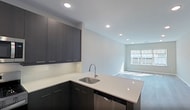 This contemporary apartment, part of The Lofts at Gloucester, offers a well-designed living space of 930 square feet. The floor plan includes two bedrooms and two bathrooms, with the primary bedroom measuring a generous 160 square feet. The open-concept layout creates a seamless flow between the living areas, enhancing the sense of space.

The kitchen is a standout feature, boasting dark wood cabinetry contrasting beautifully with stainless steel appliances and white countertops. It's equipped with a gas range, built-in microwave, and a side-by-side refrigerator, perfect for culinary enthusiasts.

Both bathrooms showcase modern design with large vanities, ample storage, and glass-enclosed showers. The dark wood cabinetry in the bathrooms echoes the kitchen's aesthetic, creating a cohesive design throughout the apartment.

Large windows in the bedrooms and living area flood the space with natural light, while also offering views of the surroundings. The light-colored walls and grey wood-look flooring contribute to the bright, airy feel of the apartment.

Storage is well-considered, with built-in closets featuring dark wood finishes that match the overall design scheme. The apartment also includes recessed lighting throughout, adding to the modern ambiance.

This apartment combines functionality with style, offering a comfortable and contemporary living space in an urban setting.