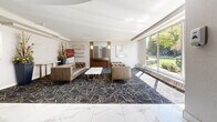 Located at 20 Esterbrooke Avenue in Toronto's M2J neighbourhood, this building lobby presents a refined and welcoming first impression. The space is defined by its dramatic double-height atrium ceiling, encircled by a curved upper-level mezzanine railing that lends a sense of grandeur and architectural distinction. Polished marble-look porcelain tile flooring in white and grey veining spans the main circulation area, reflecting light and enhancing the sense of openness.

Substantial tile-clad columns frame the central core, providing both structural definition and a sleek, contemporary aesthetic. The elevator bank, finished in warm wood-toned paneling with stainless steel doors, is conveniently positioned and clearly accessible. A dedicated rental office is also located within the lobby.

Transitioning from the entrance zone, the lounge area features a bold dark carpet with gold geometric patterning, anchoring a seating arrangement of tufted leather sofas and a marble-top coffee table. Floor-to-ceiling windows along the lounge perimeter flood the area with natural light and offer views of the surrounding greenery.

Wall-mounted sconces and contemporary pendant lighting complement the overall design. The lobby delivers a polished, functional, and inviting environment for residents and visitors alike.