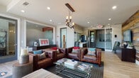 This single-floor leasing office for Venterra combines modern design with warm, inviting elements to create a professional yet comfortable environment. Visitors are welcomed through glass entry doors into a well-appointed space that seamlessly blends function with style.

The lounge area serves as the centerpiece of the space, featuring rich brown leather tufted seating — including a sofa and matching club chairs — arranged around a sleek glass coffee table. A striking sculptural chandelier with exposed Edison bulbs suspended from a reclaimed wood beam anchors the seating area, adding an industrial-chic touch. A striped area rug grounds the arrangement, while colorful accent pillows introduce pops of red and teal throughout.

The reception area is defined by a dramatic reclaimed wood accent wall in a mix of natural tones, providing a rustic contrast to the clean, modern finishes. Light wood-look flooring runs throughout, complementing the neutral palette. Floor-to-ceiling windows with slatted blinds along one wall flood the interior with natural light while offering views of the surrounding greenery.

A practical refreshment station with dark wood cabinetry, a water dispenser, and a coffee maker is conveniently tucked near the entry. Frosted glass partitions and private office rooms with glass doors provide functional separation without compromising the open, airy feel of the space. Curated artwork adds personality and polish throughout.