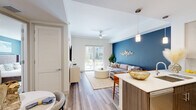 Located at 401 SE Central Pkwy in Stuart, FL, this 2-bedroom, 1-bathroom residence delivers a thoughtfully designed single-floor layout that maximizes every square foot of its compact footprint. The open-concept living and kitchen area forms the heart of the unit, where wood-look plank flooring runs seamlessly underfoot and a bold navy accent wall anchors the living space with visual depth. A ceiling fan overhead and sliding glass doors at the far end allow natural light to fill the room and provide access to an outdoor area.

The kitchen is well-appointed with two-tone cabinetry—warm wood lower cabinets paired with light upper cabinets—complemented by a marble-style tile backsplash, white quartz countertops, stainless steel appliances, and a peninsula with seating, ideal for casual dining.

The primary bedroom offers a comfortable, clean retreat with wall-mounted TV, ceiling fan, and a walk-in closet with wire shelving. The shared bathroom features a wood-toned vanity with quartz countertop, a framed mirror, and a glass-enclosed shower. Throughout, the design maintains a cohesive modern palette of whites, neutrals, and cool blues.