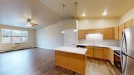 Located at 2205 Trellis Ridge Ln in De Pere, Wisconsin, this one-bedroom, one-bathroom unit offers a well-designed single-floor layout. The open-concept kitchen and living area is a defining feature, highlighted by soaring vaulted ceilings and warm hardwood-style flooring throughout. The kitchen is equipped with stainless steel appliances—including a refrigerator, range, and microwave—complemented by light wood cabinetry, a subway tile backsplash, a double sink, and a central island with a clean white countertop, illuminated by pendant lighting overhead. The living area is generously proportioned with a ceiling fan and natural light from a large window. The bedroom is a comfortable, carpeted retreat with a ceiling fan, a window with exterior views, and baseboard heating. It is accompanied by a spacious walk-in closet outfitted with multi-tiered wire shelving and hanging rods for ample storage. The bathroom features a wood-toned vanity with a granite-style countertop, a large mirror, and hardwood-style flooring. Baseboard heating is present throughout the unit, ensuring year-round comfort in Wisconsin's climate.