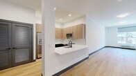 This thoughtfully designed residence at 188 Broadway in Woodcliff Lake, NJ offers a clean, modern aesthetic across a well-proportioned single-floor layout. The open-concept kitchen and living area serves as the heart of the home, featuring light wood cabinetry extending to the ceiling, sleek white quartz countertops, a breakfast bar peninsula with a matte black faucet, and a full suite of stainless steel appliances including a side-by-side refrigerator, range, and built-in microwave. Light hardwood flooring flows seamlessly throughout the entire residence, complementing the crisp white walls and dark baseboards for a contemporary, cohesive look. The spacious living area is bathed in recessed lighting and opens naturally to the rest of the home. The primary bedroom is generously sized, with large windows offering views of the surrounding neighborhood and filling the room with natural light. A flexible den provides additional space ideal for a home office or guest room. The full bathroom is elegantly appointed with wood-tone cabinetry, a white quartz double vanity, matte black fixtures, an illuminated medicine cabinet mirror, and a soaking tub with a frameless sliding glass shower enclosure. Two closets and an in-unit laundry room add practical convenience, completing this polished and move-in-ready home.