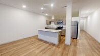 This 1-bedroom, 1-bathroom unit is thoughtfully designed across a single floor, offering a functional and modern living experience. The open-concept kitchen and living area serves as the heart of the home, featuring warm light wood flooring, recessed lighting, and a central kitchen island with a light granite countertop. The kitchen is well-equipped with taupe shaker-style cabinetry, matching granite countertops, a stainless steel refrigerator, electric range, built-in microwave, and dishwasher — providing a complete and contemporary cooking space. A long hallway with recessed lighting connects the main living area to the private quarters, leading to the spacious bedroom. The bedroom features large windows that bring in natural light and continues the warm wood flooring, creating a bright and airy feel. The bathroom is cleanly finished with matching taupe cabinetry, a granite-topped vanity, a large mirror, and the same wood flooring found throughout the unit, maintaining design continuity. A dedicated closet provides practical storage. The unit's clean white walls, consistent finishes, and cohesive material palette give the entire space a modern, move-in-ready aesthetic.
