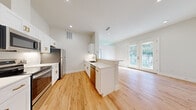 This thoughtfully designed one-bedroom, one-bathroom unit offers a clean, modern aesthetic across its efficiently utilized single floor. Light hardwood flooring runs throughout, reflecting natural light and creating a warm, cohesive ambiance.

The open-concept kitchen and living area serve as the heart of the unit. The galley-style kitchen is outfitted with white shaker cabinetry accented by brushed gold hardware, a quartz countertop, stainless steel appliances including a refrigerator, range, microwave, and dishwasher, and a deep single-basin sink with a gold-finish pull-down faucet. A peninsula with breakfast bar seating separates the kitchen from the living area, enhancing the open feel. The living space is illuminated by recessed lighting and benefits from abundant natural light streaming through French doors, which lead directly to a private balcony overlooking a tree-lined exterior.

The bedroom is a serene, well-lit retreat featuring two large windows with garden views and direct access to the full bathroom. The bathroom is finished with white marble-style tile flooring, white subway tile walls, a white vanity with under-cabinet storage, and a well-placed mirror with overhead lighting. A dedicated closet completes the unit's functional layout.