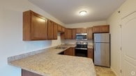 This single-floor 2-bedroom, 1-bathroom residence offers a comfortable and practical living space designed with everyday convenience in mind. The kitchen stands out as a central highlight, featuring warm honey-toned wood cabinetry that extends to the ceiling for generous storage capacity. Light granite-style countertops provide ample prep space and complement the stainless steel appliances, which include a refrigerator, an electric range, and an over-the-range microwave. A double basin sink is positioned beneath upper cabinetry, and a breakfast bar counter adds casual dining or additional workspace. The kitchen's layout is efficiently designed in a U-shape, maximizing functionality while maintaining an open feel. Light-toned flooring ties the space together and contributes to a bright, airy atmosphere throughout. The two bedrooms offer comfortable accommodations, while the single full bathroom serves the home with practicality. The overall design of the residence is clean and understated, with neutral tones and a straightforward floor plan that creates a welcoming and easy-to-maintain living environment suitable for a variety of lifestyles.