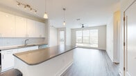Located at 2202 North Lois Avenue in Tampa, FL, this well-designed 3-bedroom, 2-bathroom residence offers a clean, modern aesthetic throughout its single-floor layout. The open-concept living and dining area is bathed in natural light from expansive floor-to-ceiling windows, offering views of the surrounding cityscape, and is accented by a ceiling fan and light hardwood-style flooring that flows seamlessly throughout the space. The contemporary kitchen is a standout feature, boasting crisp white cabinetry, a sleek gray quartz-style peninsula countertop, stainless steel appliances including a French door refrigerator, electric range, and built-in microwave, complemented by a white subway tile backsplash and stylish pendant lighting. Each of the three bedrooms is generously sized, featuring ceiling fans, large windows with outdoor views, and access to well-organized closets with wire shelving systems. The primary bedroom includes a dedicated walk-in closet and an en-suite bathroom with dark wood cabinetry, a quartz vanity, glass-enclosed shower, and wood-look tile flooring. A second full bathroom serves the remaining bedrooms. The space conveys a bright, airy atmosphere with a neutral color palette and modern finishes throughout.