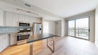 This contemporary one-bedroom, one-bathroom residence at 880 Pacific St in Stamford, Connecticut offers a well-designed layout with modern finishes throughout. Light wood-style flooring runs continuously across the entire unit, complementing the neutral warm-gray palette on the walls. The open-concept kitchen and living area forms the heart of the home, where the kitchen showcases light wood cabinetry, a white subway tile backsplash, a dark-topped island with stainless steel legs, and a full suite of stainless steel appliances including a gas range, microwave, dishwasher, and refrigerator with ice maker. Track lighting overhead adds a modern touch. The living area connects directly to a private balcony through sliding glass doors, which also frame sweeping views of a marina below. The spacious bedroom continues the floor-to-ceiling window theme, capturing the same striking waterfront scenery and filling the room with natural light. Three closets provide generous storage, including a dedicated walk-in closet with wire shelving. The bathroom features wood-look flooring, a vanity, a tiled shower, and clean, simple finishes. A hallway connects all spaces efficiently, with an in-unit laundry area adding everyday convenience to this thoughtfully appointed home.