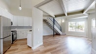 Located at 7918 Reseda Blvd in the Reseda neighborhood of Los Angeles, this two-story home offers three bedrooms, two bathrooms, and a thoughtfully designed layout spread across two floors. The main level is the larger of the two and serves as the heart of the home, featuring an open-plan kitchen and living area unified by warm light wood flooring throughout. The kitchen is outfitted with crisp white cabinetry, a subway tile backsplash, a stainless steel sink, and modern appliances. A striking fireplace anchors the living room, while exposed beam ceilings with a white-painted wood slat finish lend a mid-century architectural character and a sense of elevated volume to the space. A sleek open staircase with black metal railings connects the main level to the upper floor, where plush carpeting and a landing area with balcony access create a relaxed retreat. The balcony offers open views of the surrounding neighborhood, with palm trees and distant mountains visible on the horizon. The bedrooms are bright and airy, with natural light entering through window blinds. A dedicated closet features built-in shelving for organized storage. The bathrooms are clean and functional, with a full tub-shower combination and wood-look flooring completing the cohesive design palette found throughout the home.