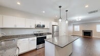 Located at 4969 W 16th St in Speedway, Indiana, this two-story home offers 2 bedrooms and 3 bathrooms thoughtfully distributed across two well-proportioned floors. The main level features an open-concept kitchen and living area, where rich hardwood-style flooring flows throughout. The kitchen is a standout, showcasing crisp white shaker cabinetry, granite countertops, a central island with pendant lighting, and a full suite of stainless steel appliances. The living area is bright and welcoming, highlighted by a classic fireplace with a tiled hearth and recessed lighting overhead. A convenient half bathroom is also found on this level. Upstairs, the spacious primary bedroom includes a walk-in closet, providing generous storage. The second bedroom is bright and well-sized, benefiting from natural light through a window with blinds. Both upper-level bathrooms are finished with granite countertops and clean white cabinetry, with one featuring a tub-shower combination with white tile surround. Additional features include a dedicated laundry area, a hallway connecting the upper rooms, and consistent neutral-toned walls throughout that lend a clean, modern aesthetic to the entire home.