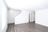 This two-floor home offers a clean, functional layout with distinct finishes across its levels. The main floor features wood-look plank flooring throughout the living area, which is bright and open with a staircase leading to the upper level. The galley-style kitchen is well-equipped with ample cabinetry featuring warm wood-tone accents, a double-basin sink, a range, and a full-size refrigerator, with additional counter and storage space running along both sides of the room. A full bathroom on this level includes a single-vanity with under-sink storage, a toilet, and a tub-shower combination, all finished with durable wood-look flooring. Upstairs, the bedrooms are carpeted in a neutral tone and feature vaulted ceilings with ceiling fans, lending each room an airy, spacious feel. Natural light enters through windows fitted with blinds. The bedrooms include closets with hanging rods for convenient storage, and one room offers access to an additional adjoining space. Throughout the home, the neutral white and beige color palette creates a versatile, move-in-ready environment suited to a variety of interior styles.