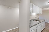 This two-bedroom, one-bathroom residence in Colorado Springs, CO offers a well-organized single-floor layout designed for comfortable everyday living. The combined dining and kitchen area features white cabinetry with brushed nickel hardware, granite-look countertops, a stainless steel sink, and wood-look flooring that flows through the main living spaces. A pendant light fixture anchors the transition between the dining and living areas, where plush carpeting and a sliding glass door lead to a private balcony with outdoor views. The living room is generously proportioned, bathed in natural light, and finished with textured ceilings throughout. Both bedrooms are carpeted and offer dedicated closet space, with the spacious primary bedroom providing ample room for furniture arrangements. The full bathroom includes a soaking tub with tiled surround, a vanity with storage, and the same wood-look flooring found in the main areas. A hallway connects the private spaces, accompanied by additional closet storage. A utility room adds functional convenience. Neutral tones and clean finishes give the entire unit a bright, move-in-ready feel.