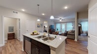 This thoughtfully designed single-floor residence offers a seamless open-concept layout connecting the kitchen, dining, and living areas. The kitchen is a standout feature, showcasing granite countertops, dark espresso cabinetry, stainless steel appliances including a refrigerator and dishwasher, and a central island with a double-basin sink illuminated by pendant lighting. Wood-look flooring extends throughout the main living areas, adding warmth and continuity to the space.

The living room is bright and inviting, benefiting from natural light that streams through large French doors leading to an outdoor area. A ceiling fan completes the comfortable atmosphere. The dining area sits adjacent, creating a natural flow ideal for entertaining.

The primary bedroom is generously sized with plush carpeting, a ceiling fan, and ample natural light from a window with blinds. It connects directly to a full bathroom featuring granite countertops, dark cabinetry, tile flooring, and access to a spacious walk-in closet outfitted with dual wire shelving systems. A second bedroom, also carpeted and well-lit, is served by an additional bathroom that mirrors the same refined finishes found throughout the home. The consistent use of neutral tones and quality materials creates a cohesive, modern aesthetic across every room.