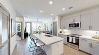 Located in Leander, TX, this thoughtfully designed one-bedroom, two-bathroom residence offers an efficient and modern layout. The open-concept kitchen and living area serves as the heart of the home, anchored by a large white quartz island with an integrated sink and bar seating — ideal for casual dining or entertaining. The kitchen is outfitted with gray shaker-style cabinetry, a classic subway tile backsplash, stainless steel appliances including a range, microwave, and refrigerator, and light wood-look flooring that extends throughout the main living areas. The living room is bright and welcoming, featuring large windows with horizontal blinds and sheer curtains, a ceiling fan, and access to an outdoor balcony that brings in generous natural light. The bedroom is a calm retreat finished with plush carpet, a ceiling fan, and a sizable window with outdoor views. A walk-in closet with built-in shelving and dual hanging rods provides practical storage. The bathrooms include a soaking tub with a tiled surround and a curved shower rod. Clean white walls, recessed lighting, and a neutral color palette throughout give the space a cohesive, contemporary feel.